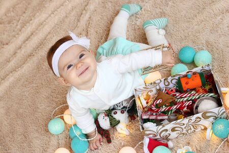 Beautiful smiling little girl in blue and white dress is lying on a beige plaid, playing with...