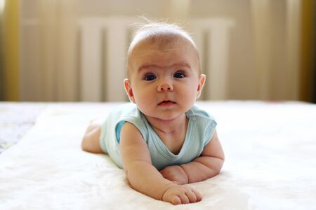 Little cute baby girl is trying to crawl on a bed at home.の写真素材