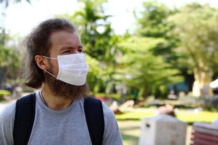 European man is walking in summer tropical park with medical face mask for protect himself from coronavirus disease, influenza virus and other infections.の写真素材
