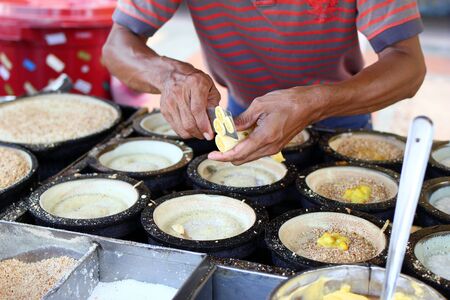 Unrecognizable man is cooking traditional Malaysian street food apam balik - thick soft pancake with...
