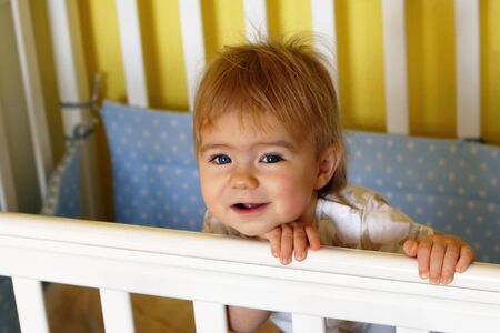 Happy one year old girl with blue eyes and blond after waking up in the morning in her bed.の写真素材