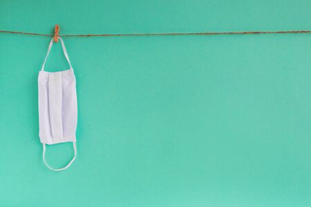 Drying of medical face mask after washing on a rope for reuse, on a turquoise background. Concept of new normal lifestyle.の写真素材