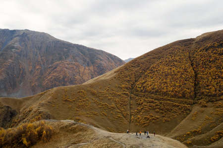 Colorful autumn landscape in cloudy weather with walking tourists. Caucasus Mountains, Georgia.