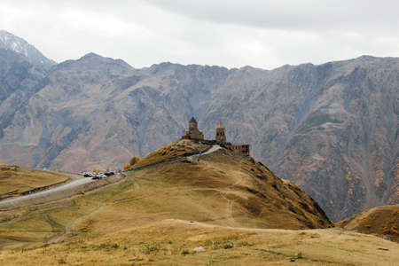 Colorful autumn landscape with Gergeti Trinity Church on a background of Caucasus Mountains,...
