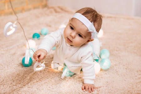 Curious little girl in blue and white dress is holding wire of electricity Christmas lights and playing with them.の写真素材