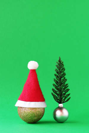 Christmas decorations - shiny gold and silver balls with Christmas tree and Santa Claus red hat tree on green background with copy space.の写真素材