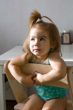 Candid lifestyle portrait of adorable baby girl with blond hair. Sunny morning at home.