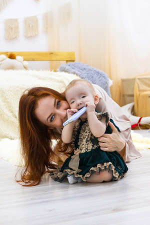Mother and little daughter are playing with mobile phone. Happy family time at home.の写真素材