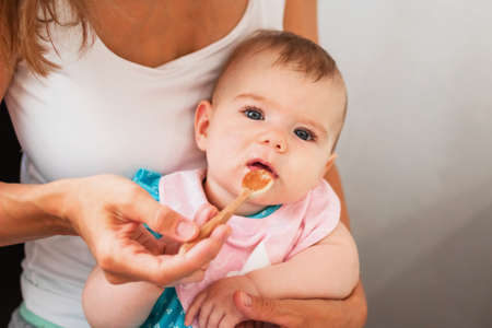 Mother feeding cute baby girl vegetable puree from a spoon. Healthy eating nutrition for little kidsの写真素材