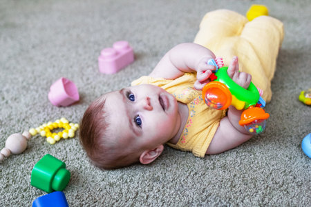 Cute little baby girl lying on a floor and playing with colorful plastic and wooden toys. Develop child motor skills.の写真素材