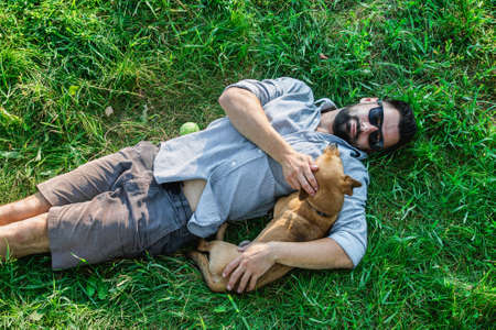 Top view of man and dog lying on green grass. Attractive European man is hugging his dog.の写真素材