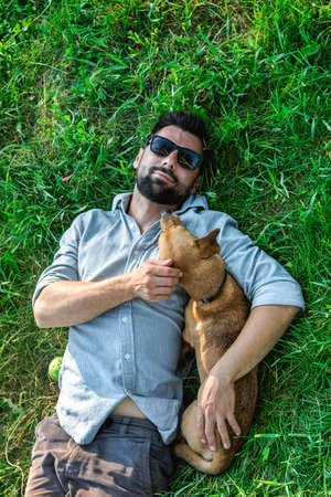 Top view of man and dog lying on green grass. Attractive European man is hugging his dog.の写真素材