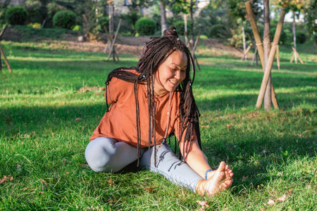 Beautiful young woman with long African braids is doing yoga outside in a park. Concept of healthy...