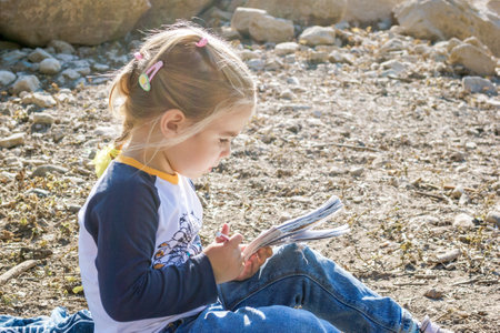 Young girl enjoying a peaceful moment by the lake while immersed in a captivating bookの写真素材