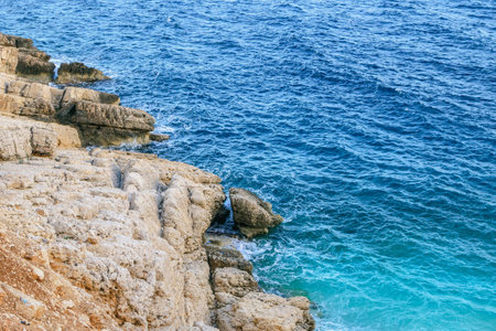 Small waves gently lap the shore under the bright sun. Clear blue-green waters, light gray rocks, sandy beaches, a serene and secluded oasis with only a few people enjoying the peaceful scenery.の写真素材