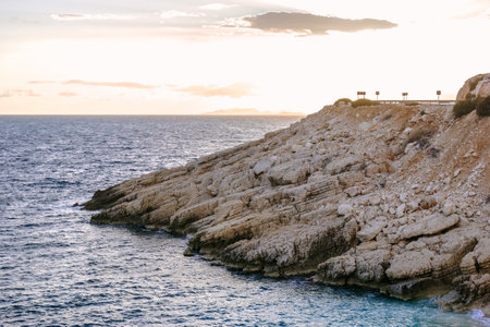 Road on a cliff near to sea at the sunset. Demre, Turkey. Rocky beach in the Mediterranean sea with clear blue water and stones.の写真素材