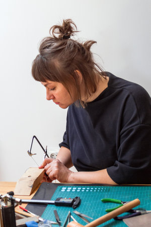 Focused jeweler woman sawing metal sheet with a coping saw in the home workshop.