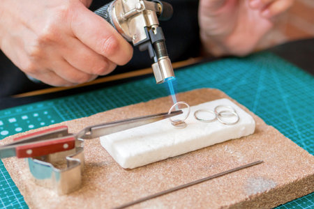 A woman uses a blowtorch to create jewelry on a on a worktable with cutting mat.の写真素材