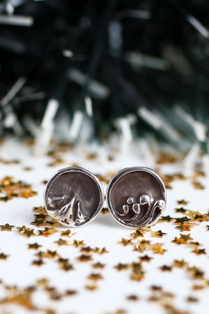 Handmade round silver earrings with nature-inspired design on white sparkly Christmas background.