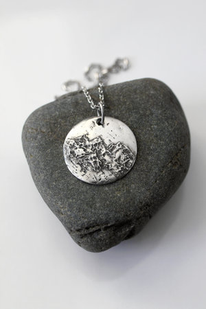 Handmade round silver pendant with a unique and textured surface on a rock and white background.の写真素材