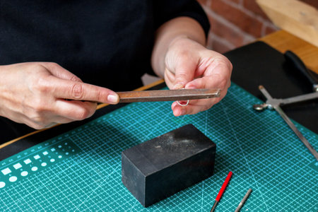 Woman-jeweler is carefully crafting a silver ring during jewelry design process in workplace.