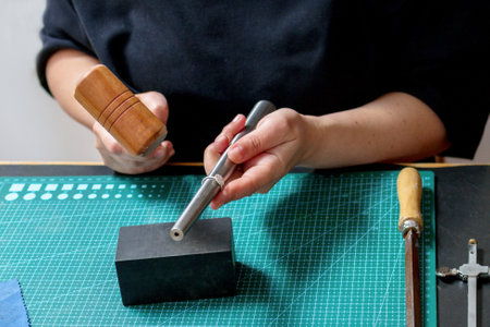 A woman in a black shirt is skillfully hammering a metal rod onto a sturdy steel block, wearing...