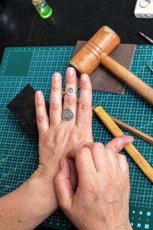 Female hands with a silver ring and pendant in moon shape on a background of jewelry workplace.