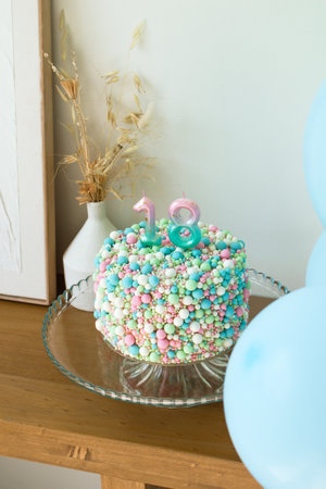 Celebratory 18th Birthday Cake with Colorful Sprinkles and Candles on a Glass Stand.の写真素材