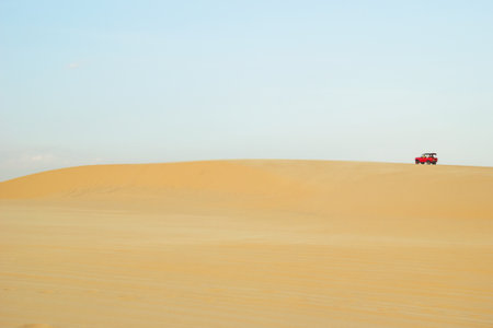 Vibrant Red Off-Road Vehicle Navigating a Vast Expanse of Golden Sand. Mui Ne, Vietnam, White Dunes.の写真素材