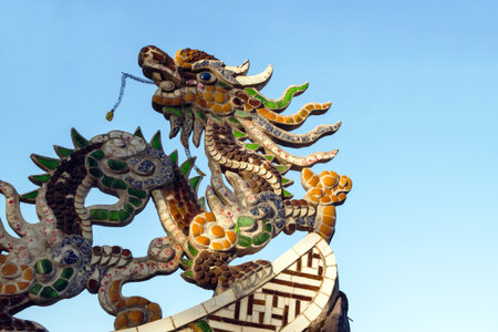 Magnificent Dragon Sculpture Adorning a Temple Roof Against Clear Blue Sky Backdrop. Dalat, Vietnam.の写真素材