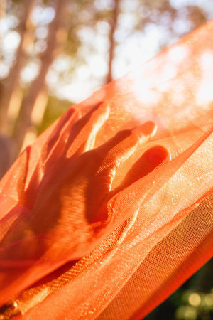 Hand Touches Soft Orange Fabric Sunlit Texture and Gentle Connection, Summer Warmth.の写真素材