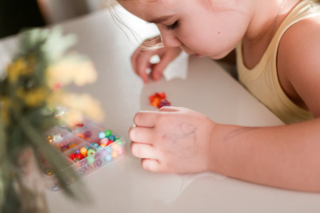 Little Girl is Concentrating on Crafting Colorful Jewelry with Beads at Home, Creative Activity.の写真素材