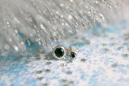 Handmade silver heart-shaped stud earrings with green gemstones on a Christmas sparkly background.の写真素材