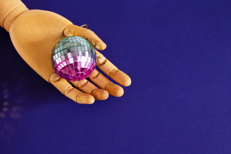 Wooden Hand Holding Shiny Disco Ball on Blue Background. Retro Party, Celebration Concept.の写真素材