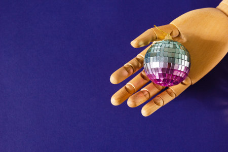 Wooden Hand Holding Colorful Disco Ball on Purple Background with Copy Space. Christmas Decorations.の写真素材