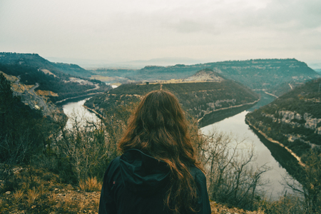 Girl from behind looking at the two roads of the meander of a river on a cloudy dayの写真素材