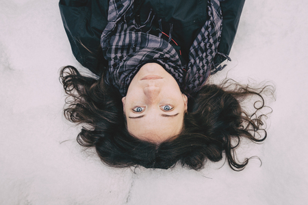 Blue-eyed girl lying on top of snow looking at camera happyの写真素材