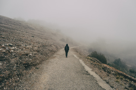 Girl walking on her back on a mountain road with a lot of fogの写真素材