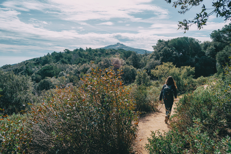 Woman walking in the distance on a trail among mountains on a sunny dayの写真素材
