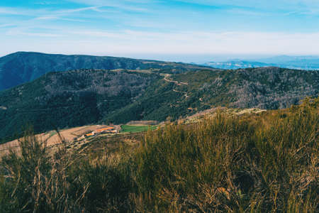 Landscape with views of green wooded mountains with a few houses and a path