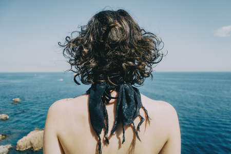 A girl with a kerchief on her neck and her back naked from behind looking at the horizon in the seaの写真素材