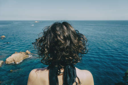 A girl with a kerchief on her neck and her back naked from behind looking at the horizon in the seaの写真素材