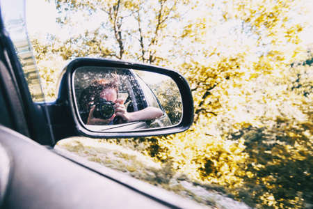Selfie of a girl in the rear view of the car while the car is running. The girl wears her hair tied up and blows her away with the wind.の写真素材