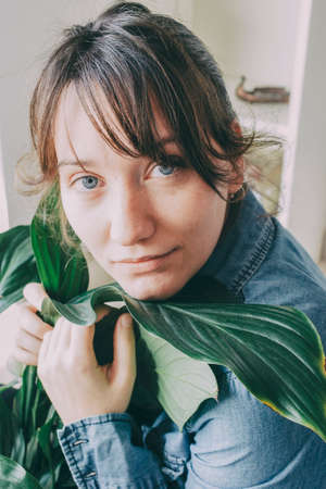 portrait of a woman with brown hair sits on the floor of her house and hugs a plant from a potの写真素材