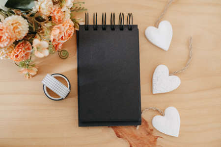 notebook with black sheets with copy space, on a wooden table with a bouquet of flowers and a white heart.の写真素材