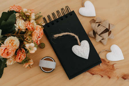 notebook with black sheets with copy space, on a wooden table with a bouquet of flowers and a white heart.の写真素材