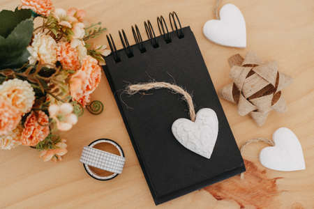 notebook with black sheets with copy space, on a wooden table with a bouquet of flowers and a white heart.の写真素材