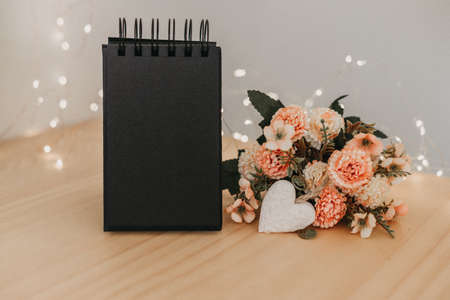 notebook with black sheets with copy space, on a wooden table with a bouquet of flowers and a white heart and bokeh lights around it.の写真素材