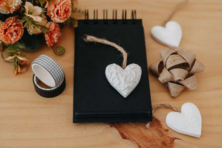 notebook with black sheets with copy space, on a wooden table with a bouquet of flowers and a white heart.の写真素材