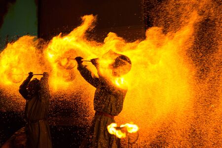 Fire show: two people in protective suits twist coal props over their heads, spreading sparks around themselvesの写真素材